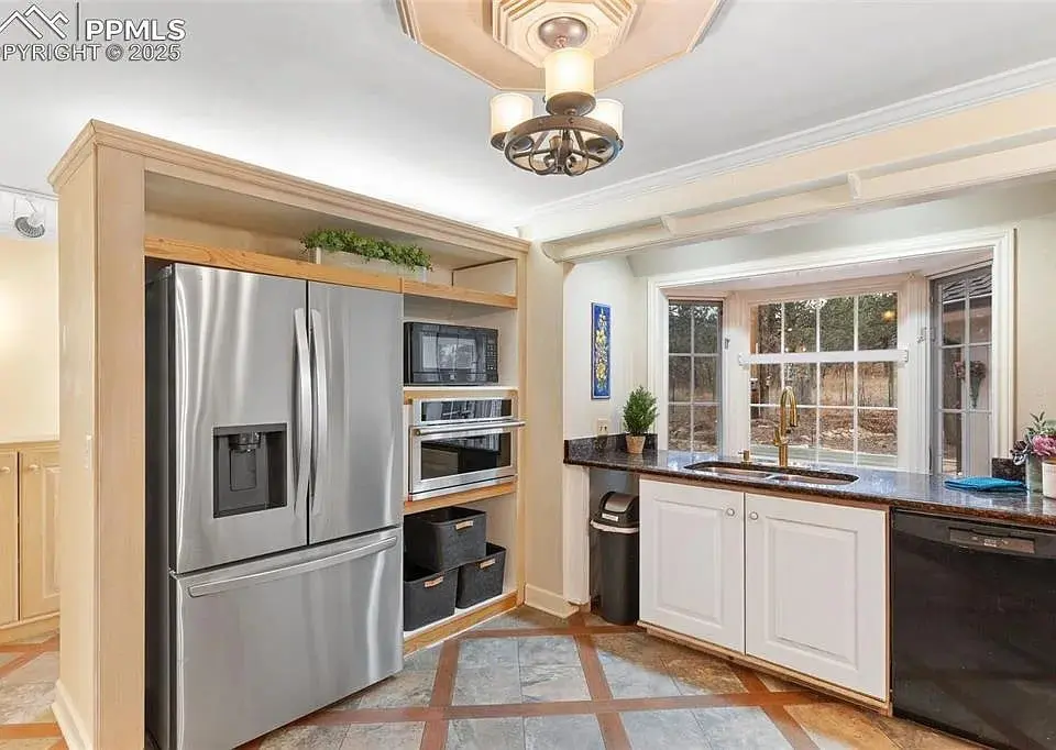 Modern kitchen with stainless steel appliances, large window, and dark countertops.