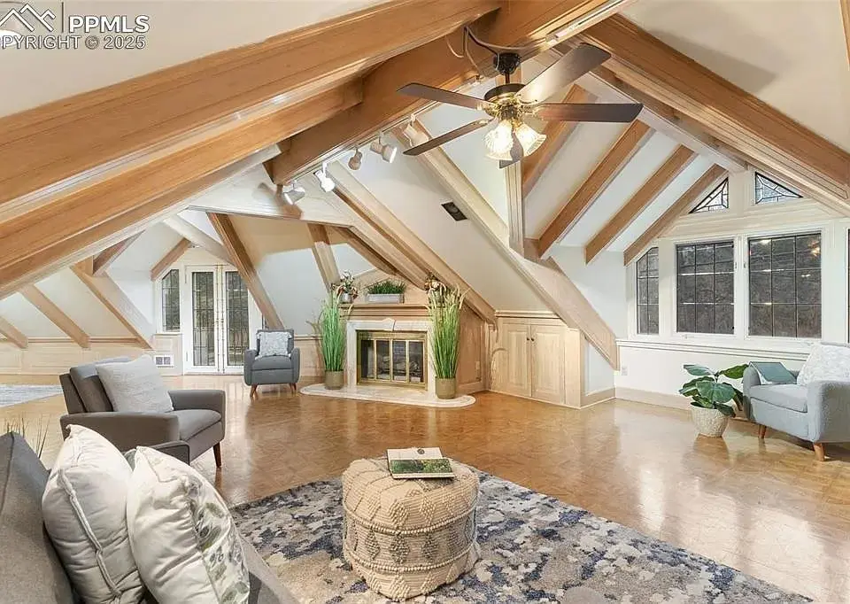 Spacious attic living room with wooden beams, fireplace, seating area, and large windows.