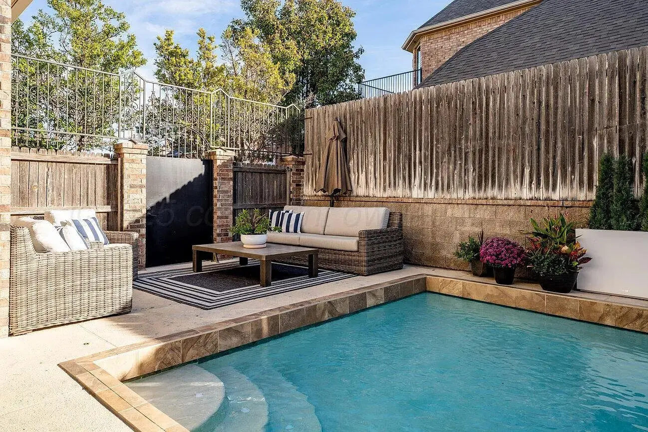 Cozy outdoor patio with wicker furniture, a striped rug, and a small pool.