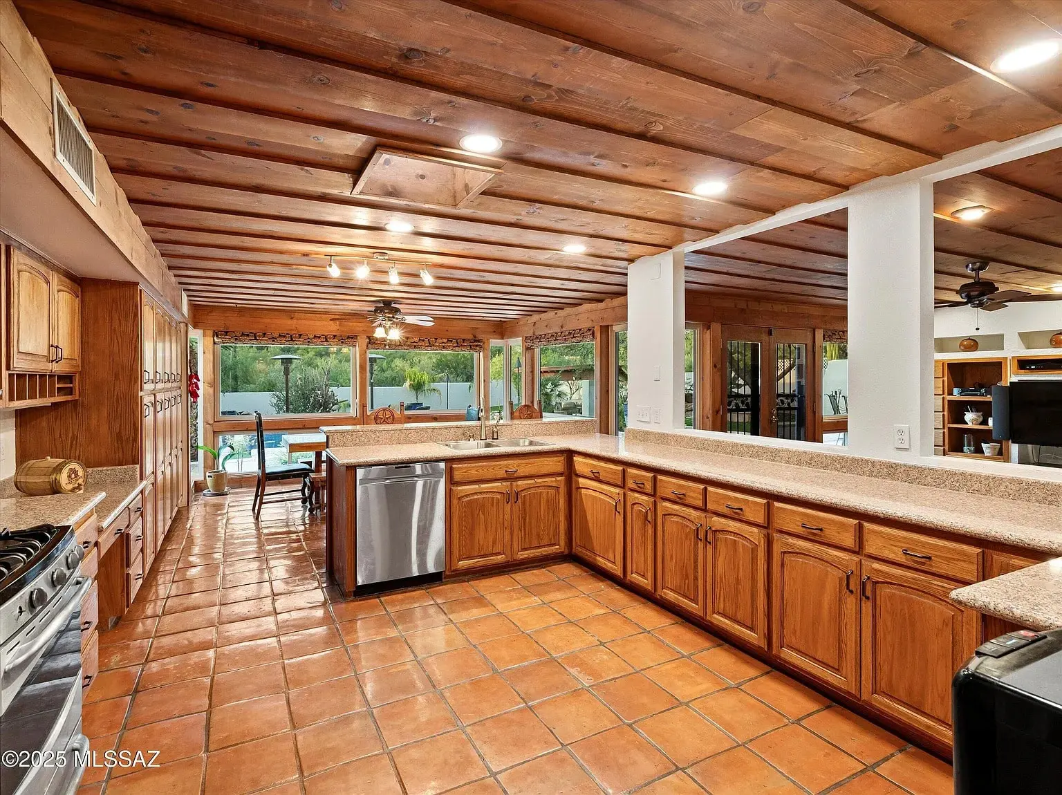 Spacious kitchen with wooden cabinets, tile flooring, and large windows overlooking a pool area.