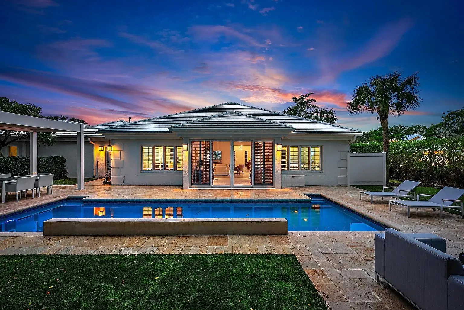 Modern house with a pool, patio furniture, and a vibrant sunset sky in the background.