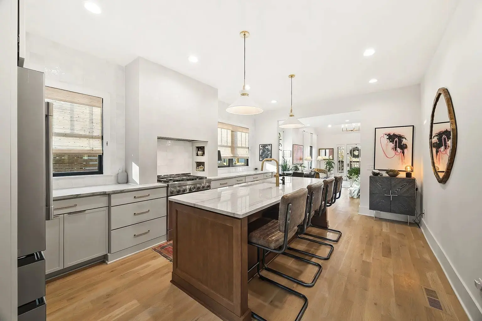 Modern kitchen with a large island, bar stools, pendant lights, and wooden flooring.