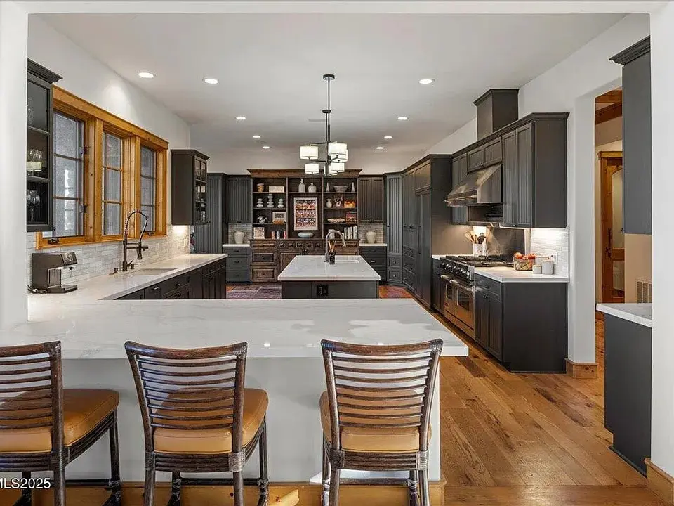 Modern kitchen with dark cabinets, white countertops, island, bar stools, and wooden flooring.