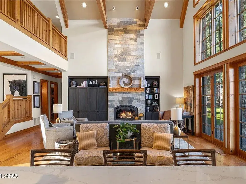 Spacious living room with high ceilings, stone fireplace, large windows, and wooden beams.
