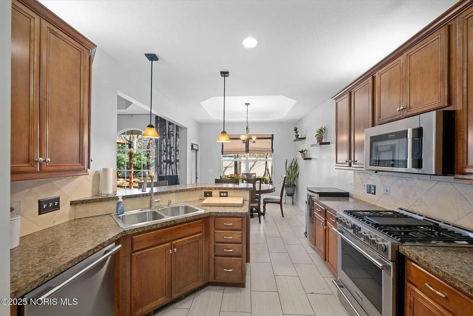 Modern kitchen with wooden cabinets, stainless steel appliances, and a dining area in the background.