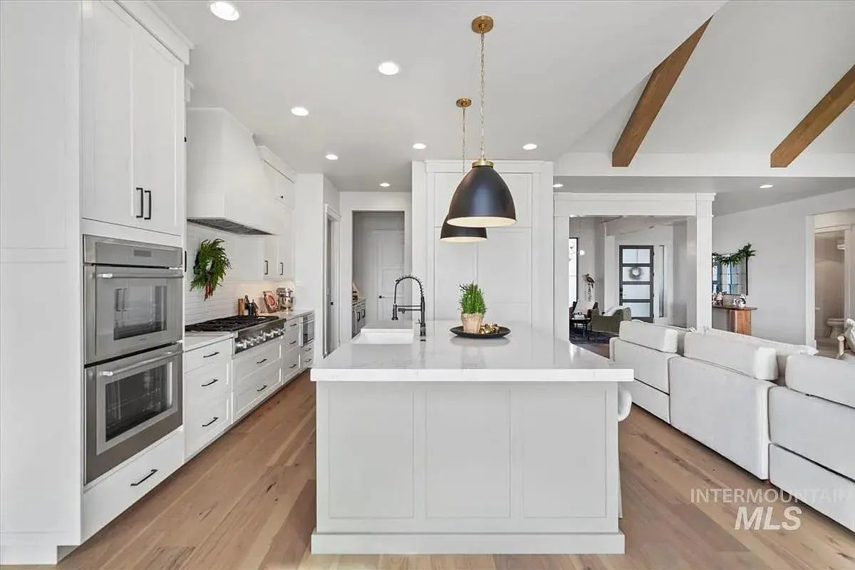 Modern kitchen with white cabinets, large island, pendant light, and wooden beams on the ceiling.