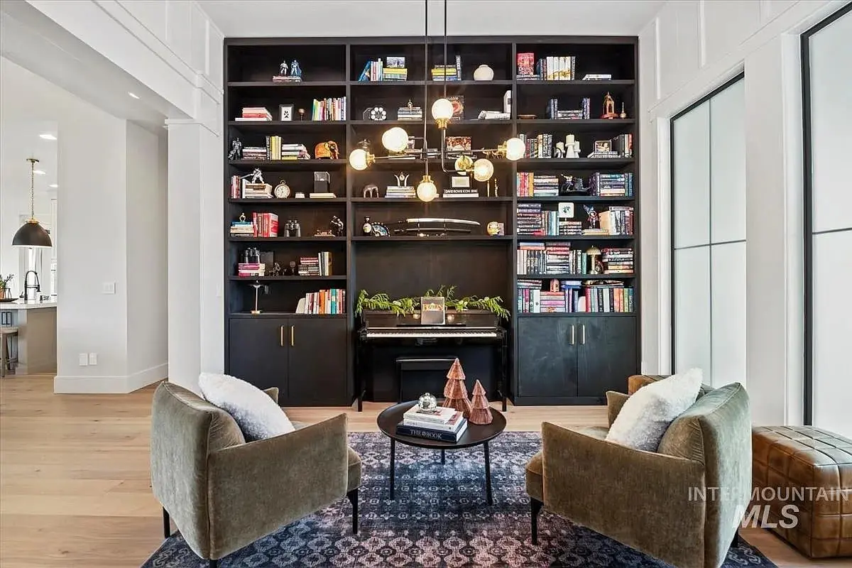 Cozy reading nook with two chairs, a piano, and a large bookshelf filled with books.