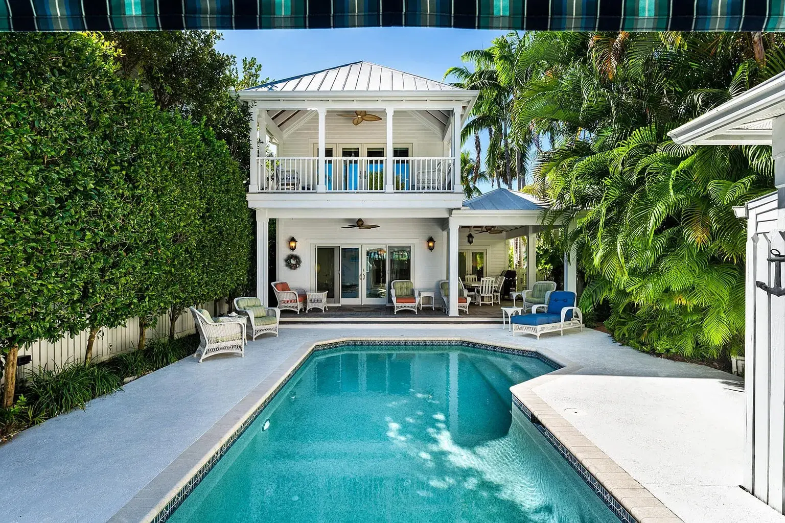 Two-story house with a pool, surrounded by lush greenery and outdoor seating.