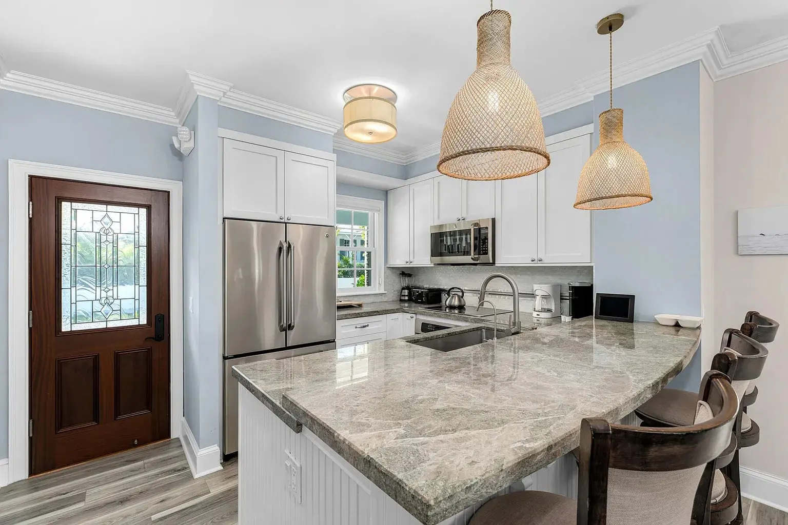 Modern kitchen with marble countertops, stainless steel appliances, and pendant lighting over a breakfast bar.