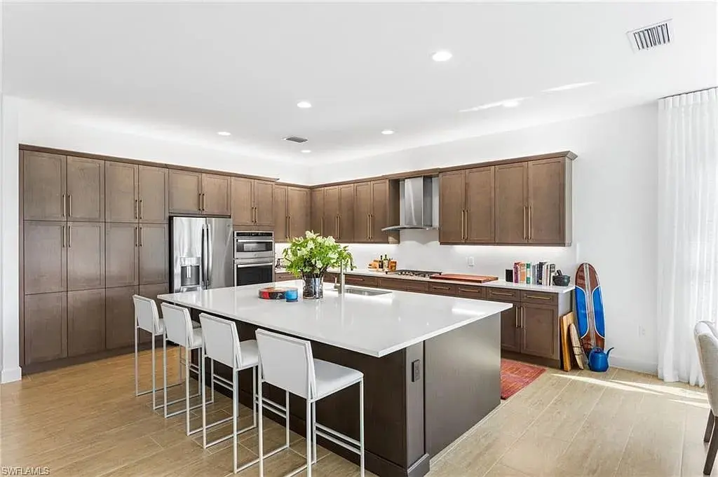 Modern kitchen with dark wood cabinets, white island, stainless steel appliances, and four white bar stools.