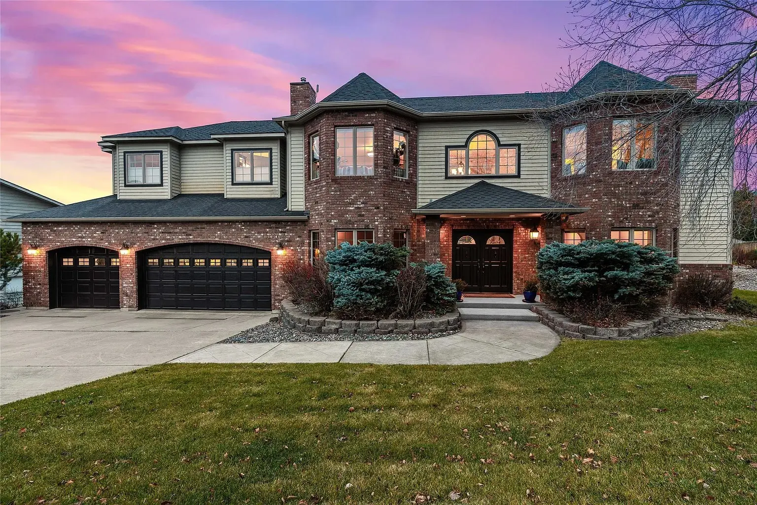 Two-story brick and siding house with three-car garage at sunset.