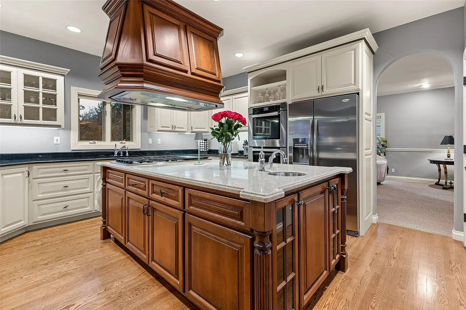Spacious kitchen with wooden island, stainless steel appliances, and a vase of red roses.