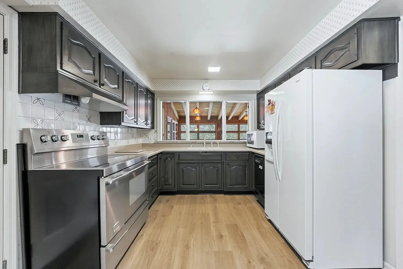 Modern kitchen with dark cabinets, stainless steel appliances, white refrigerator, and wood flooring.