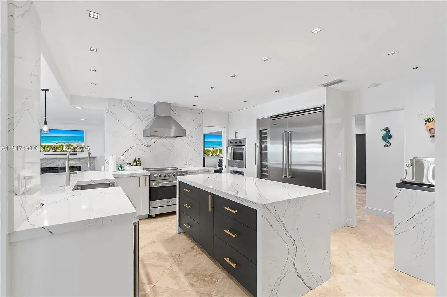 Modern kitchen with marble countertops, large island, stainless steel appliances, and bright natural lighting.