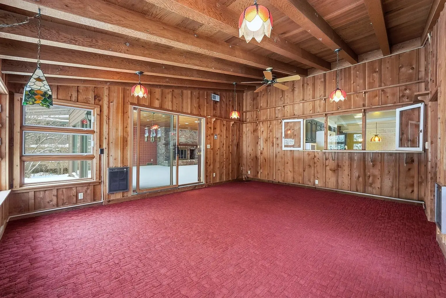 Room with wooden walls and ceiling, red carpet, and stained glass pendant lights. Large windows and sliding door.