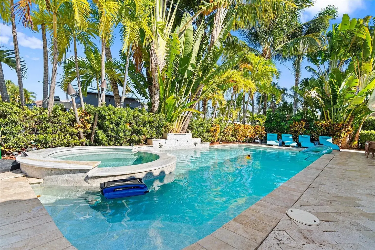 Luxurious backyard pool with attached hot tub, surrounded by palm trees and lounge chairs.