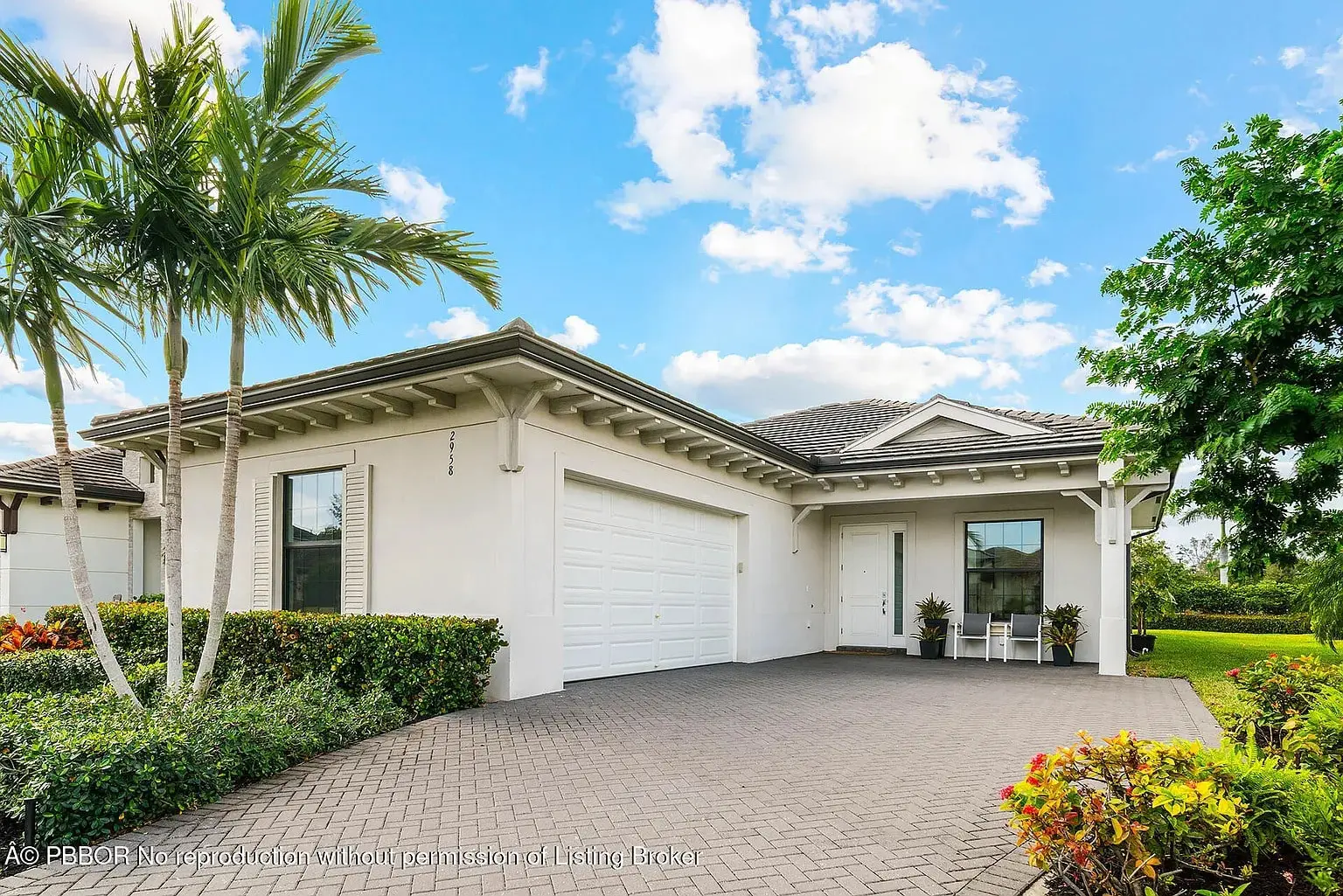 Single-story white house with a two-car garage, palm tree, and a paved driveway.