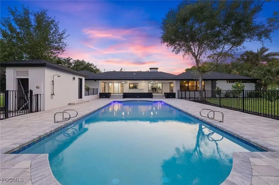 Backyard view of a modern house with a large swimming pool at sunset.