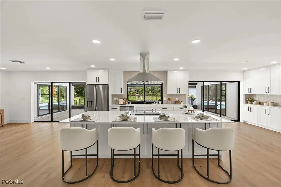 Modern kitchen with large island, bar stools, white cabinets, and sliding glass doors leading outside.