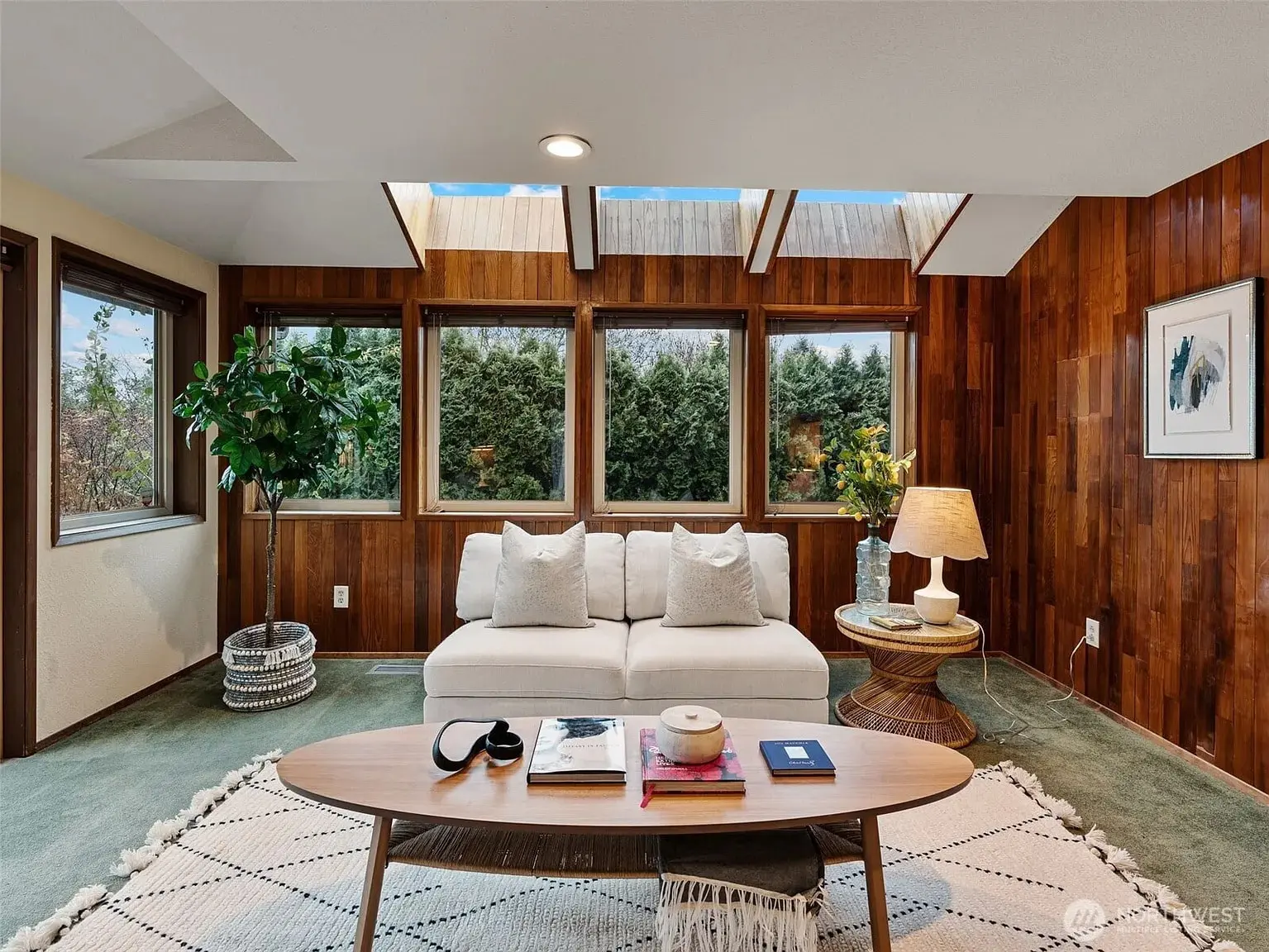A cozy living room with a white sofa, wooden walls, skylights, and a coffee table.