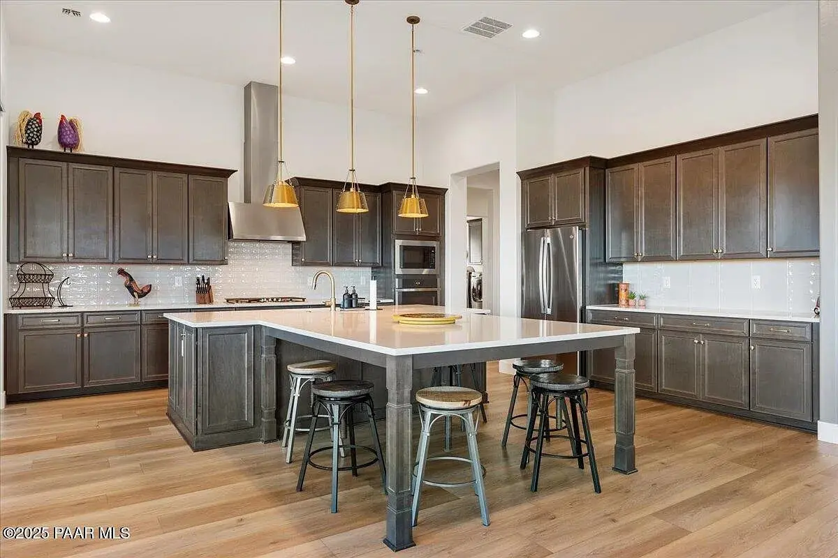 Modern kitchen with dark wood cabinets, large island, pendant lights, and stainless steel appliances.