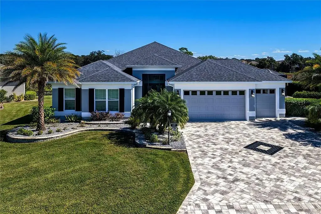 Single-story house with a gray roof, palm trees, and a paved driveway.