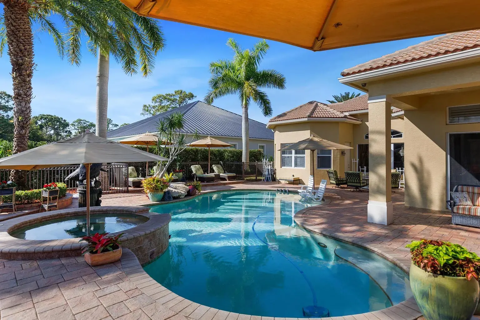 Backyard with a swimming pool, hot tub, patio furniture, and tropical plants under a clear blue sky.