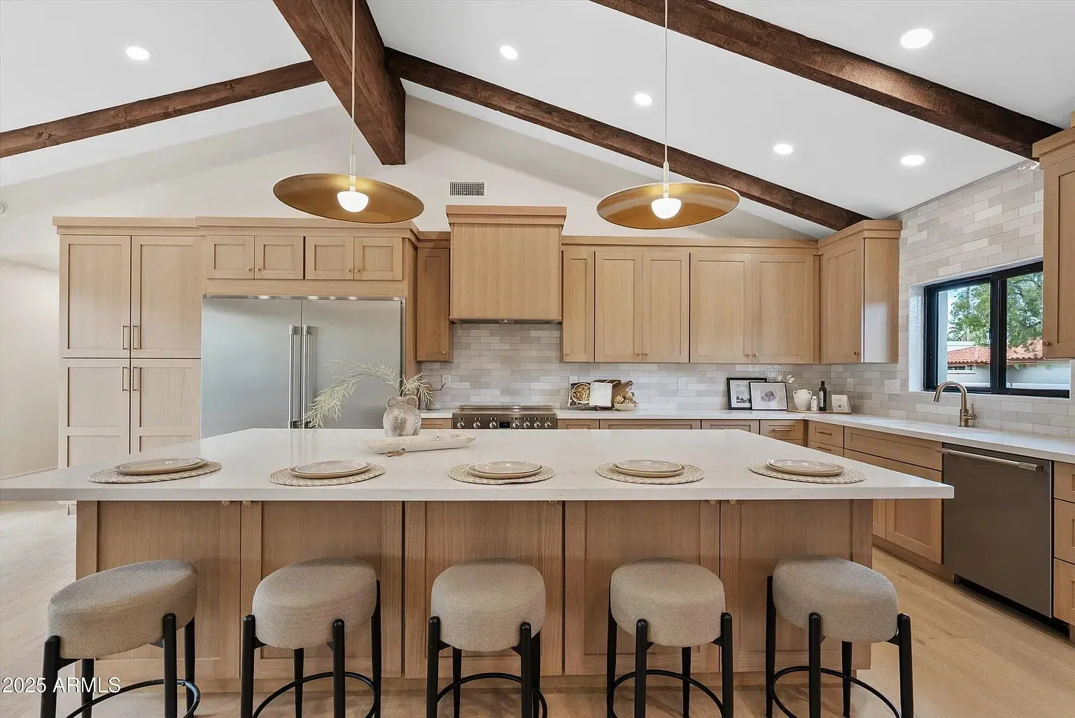 Spacious kitchen with wooden cabinets, large island, barstools, and exposed beams on the ceiling.