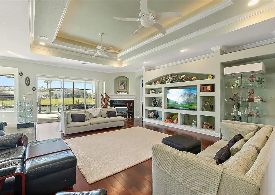 Spacious living room with sofas, large TV, ceiling fans, and glass display cabinets.