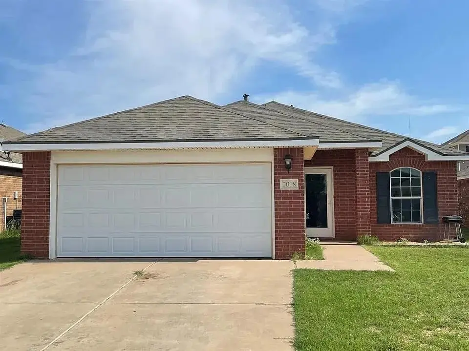 Single-story red brick house with a two-car garage and a small front yard.