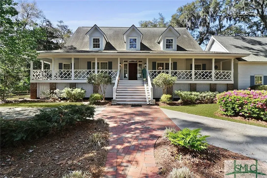 Two-story house with a large porch, surrounded by trees and a brick walkway.