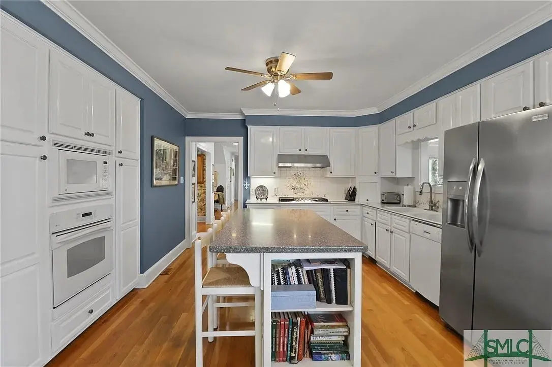 Spacious kitchen with white cabinets, blue walls, island with books, and stainless steel appliances.