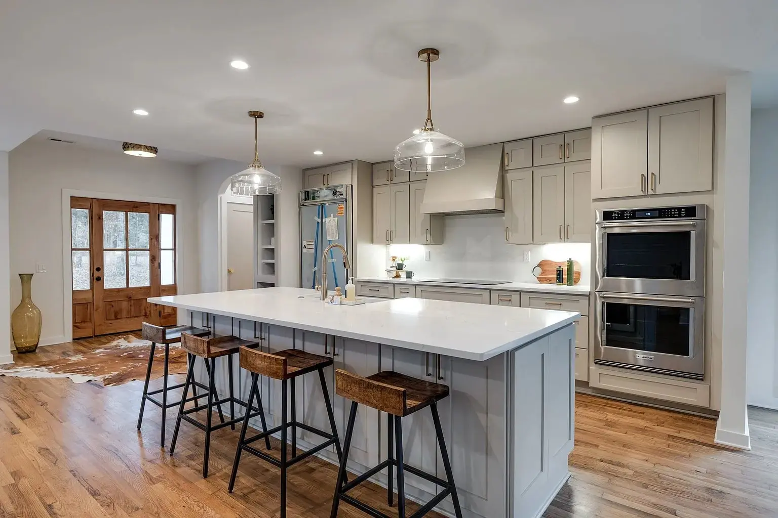 Modern kitchen with a large island, bar stools, stainless steel appliances, and wooden flooring.