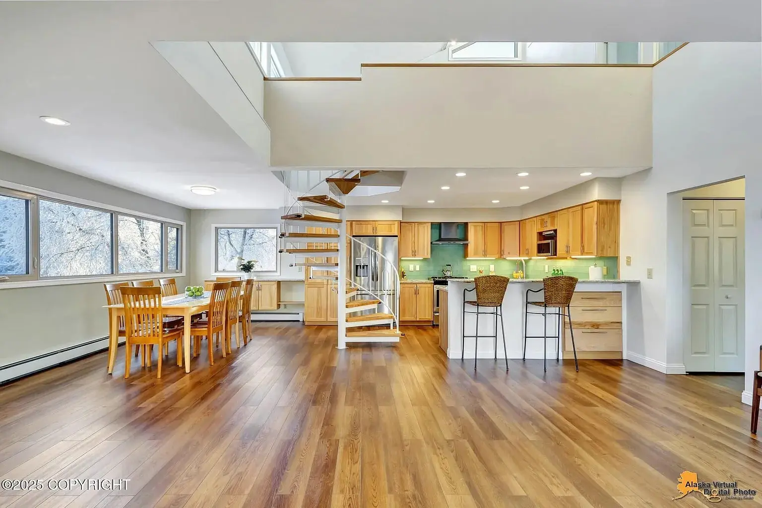Open-concept kitchen and dining area with wooden floors, spiral staircase, and large windows.