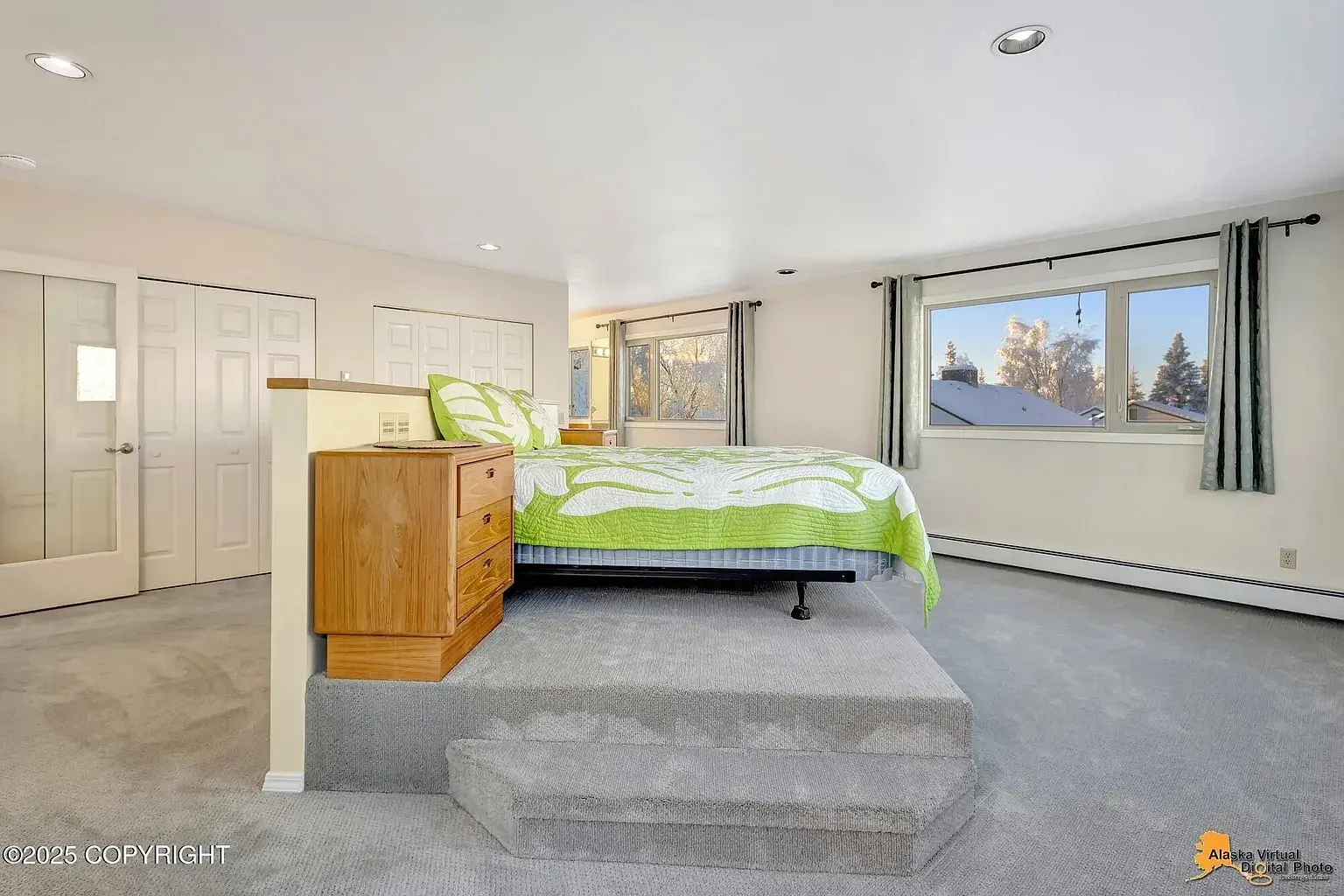 Bedroom with a raised bed platform, green and white bedding, large window, and carpeted floor.