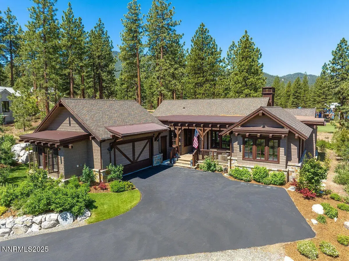 Aerial view of a rustic house with a wooden exterior, surrounded by trees and a paved driveway.