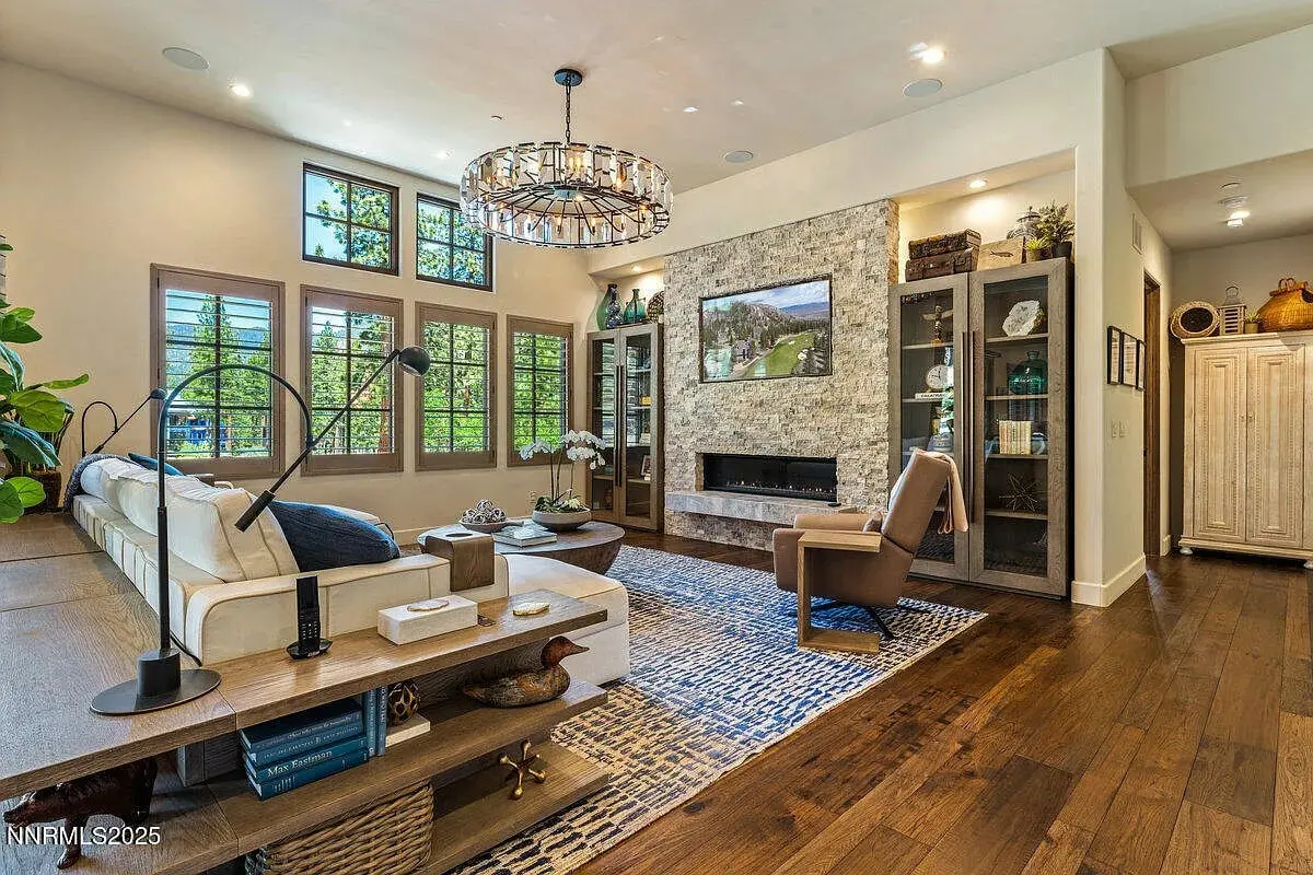 Modern living room with large windows, stone fireplace, and elegant furniture. Warm, inviting atmosphere.