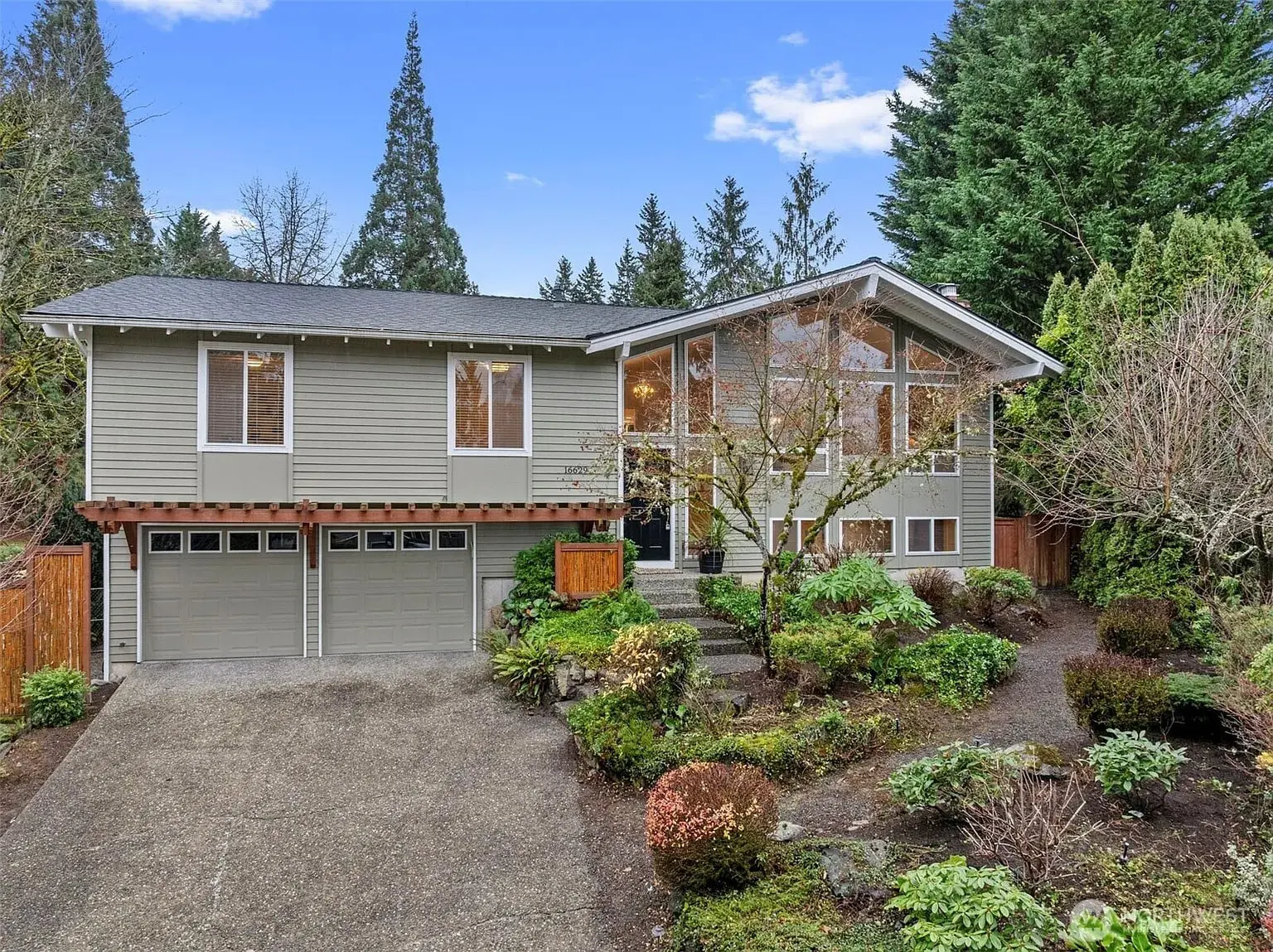 Two-story house with large windows, surrounded by trees and landscaped garden.