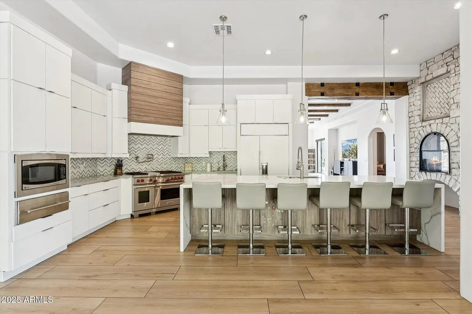 Modern kitchen with white cabinets, wood accents, island with bar stools, and stainless steel appliances.