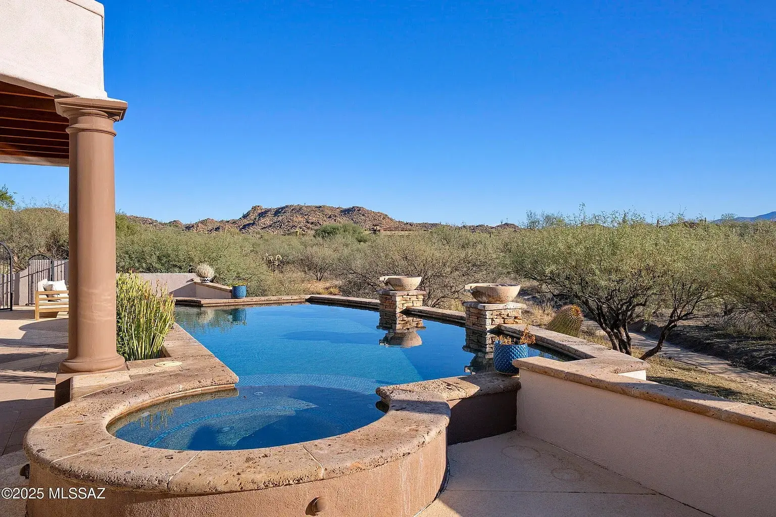 Outdoor infinity pool with a hot tub, overlooking desert landscape and distant mountains.