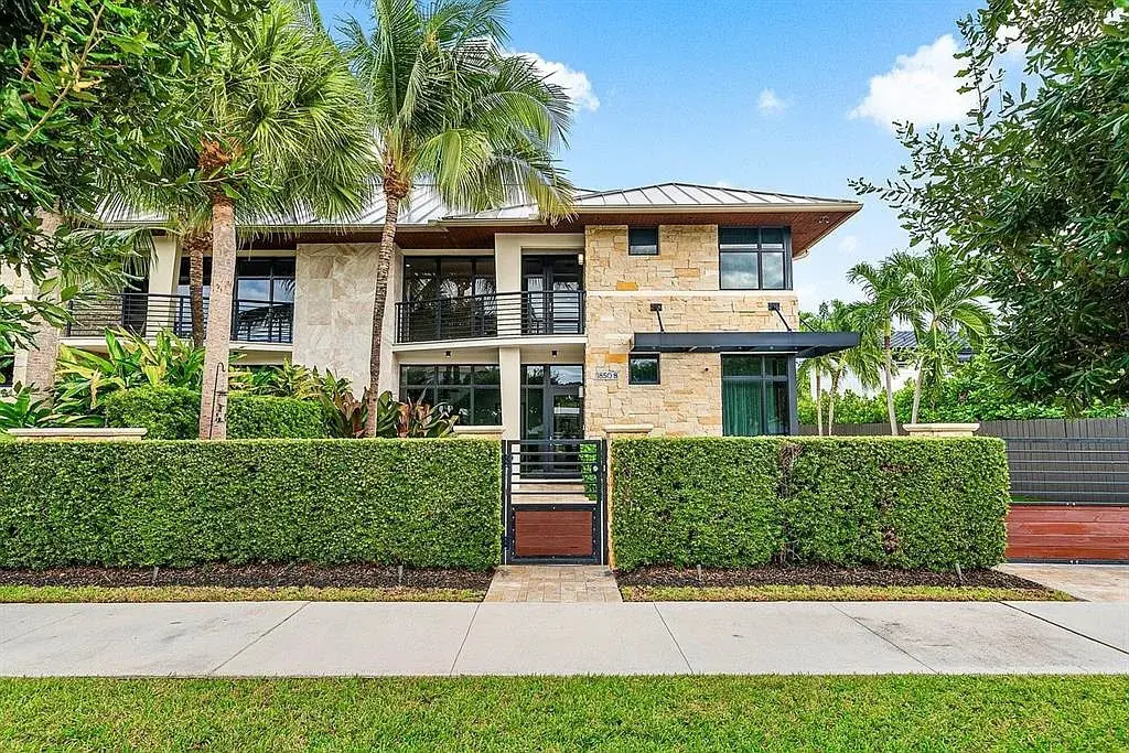 Modern two-story house with stone facade, palm trees, and a neatly trimmed hedge in front.