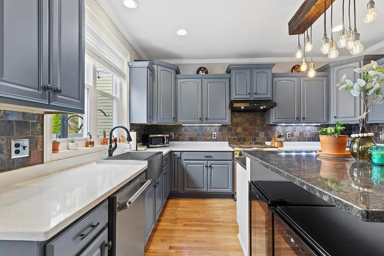 Modern kitchen with gray cabinets, farmhouse sink, and hanging light bulbs over a black countertop.