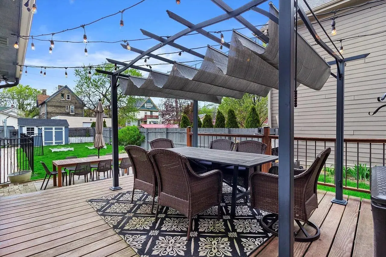 Outdoor patio with wicker chairs, table, pergola, string lights, and a patterned rug.