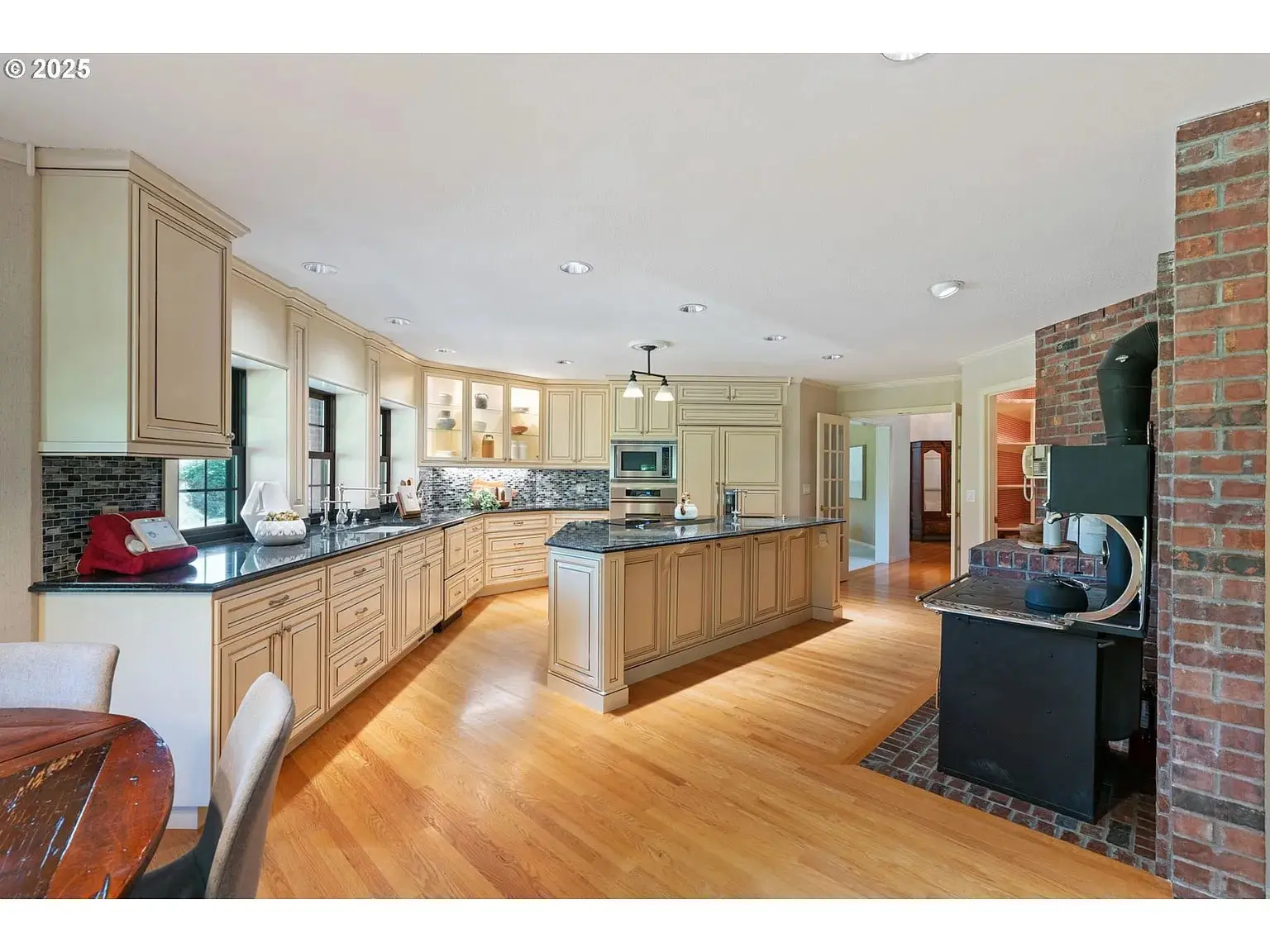 Spacious kitchen with light wood cabinets, island, brick accent wall, and hardwood floors.