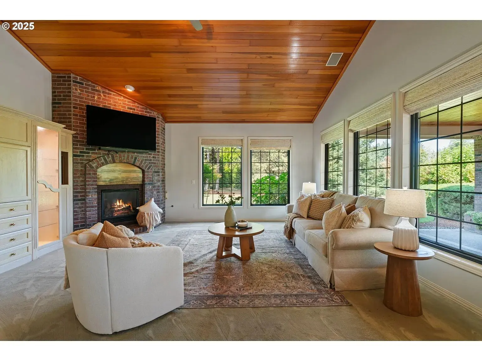 Cozy living room with fireplace, wooden ceiling, large windows, and comfortable seating.