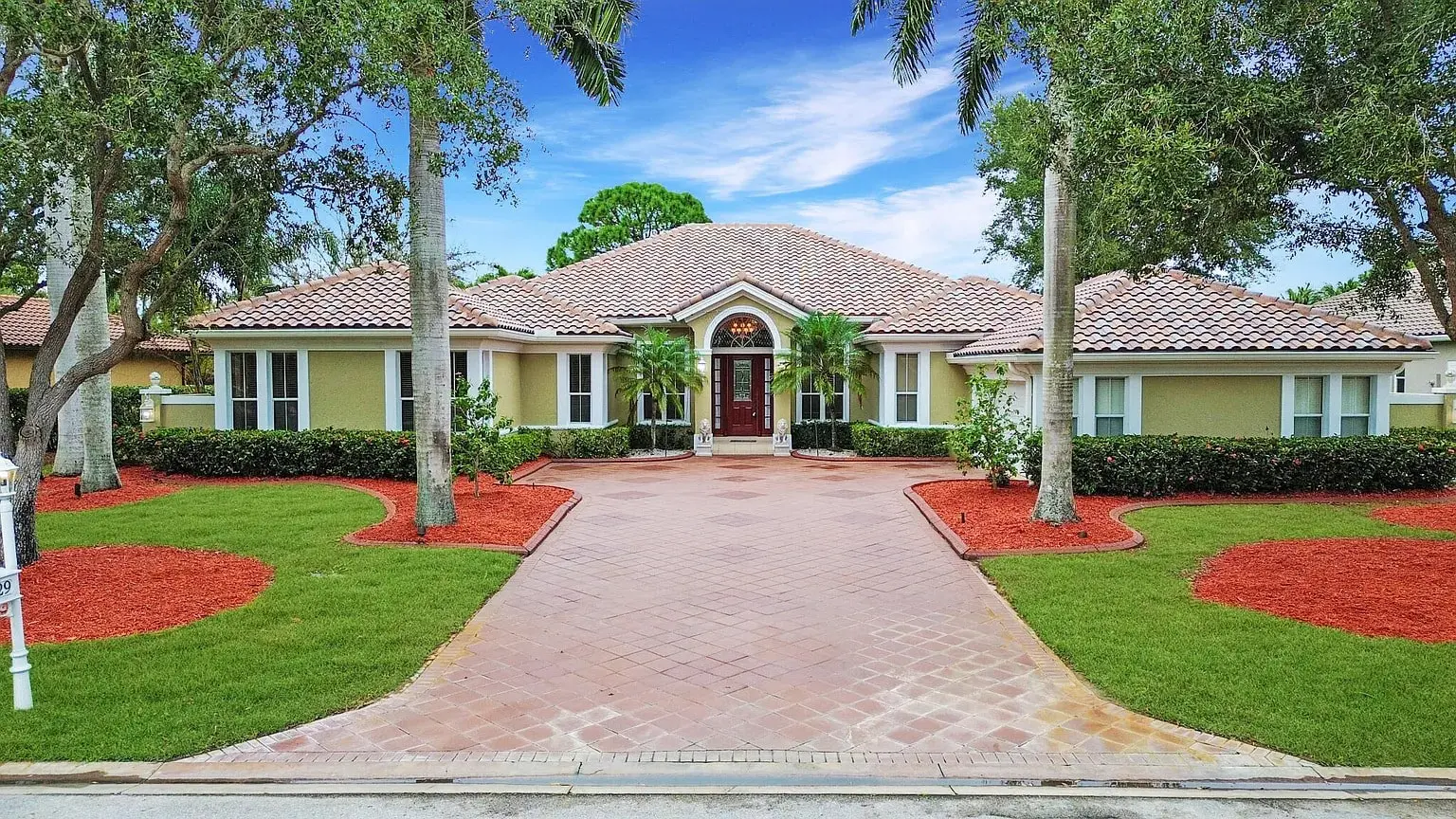 Single-story house with a tiled roof, surrounded by trees and landscaped with red mulch.
