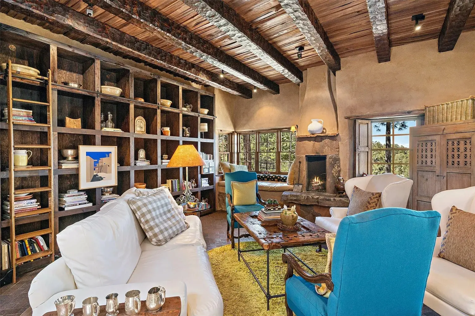 Cozy living room with wooden beams, bookshelves, fireplace, and colorful seating.