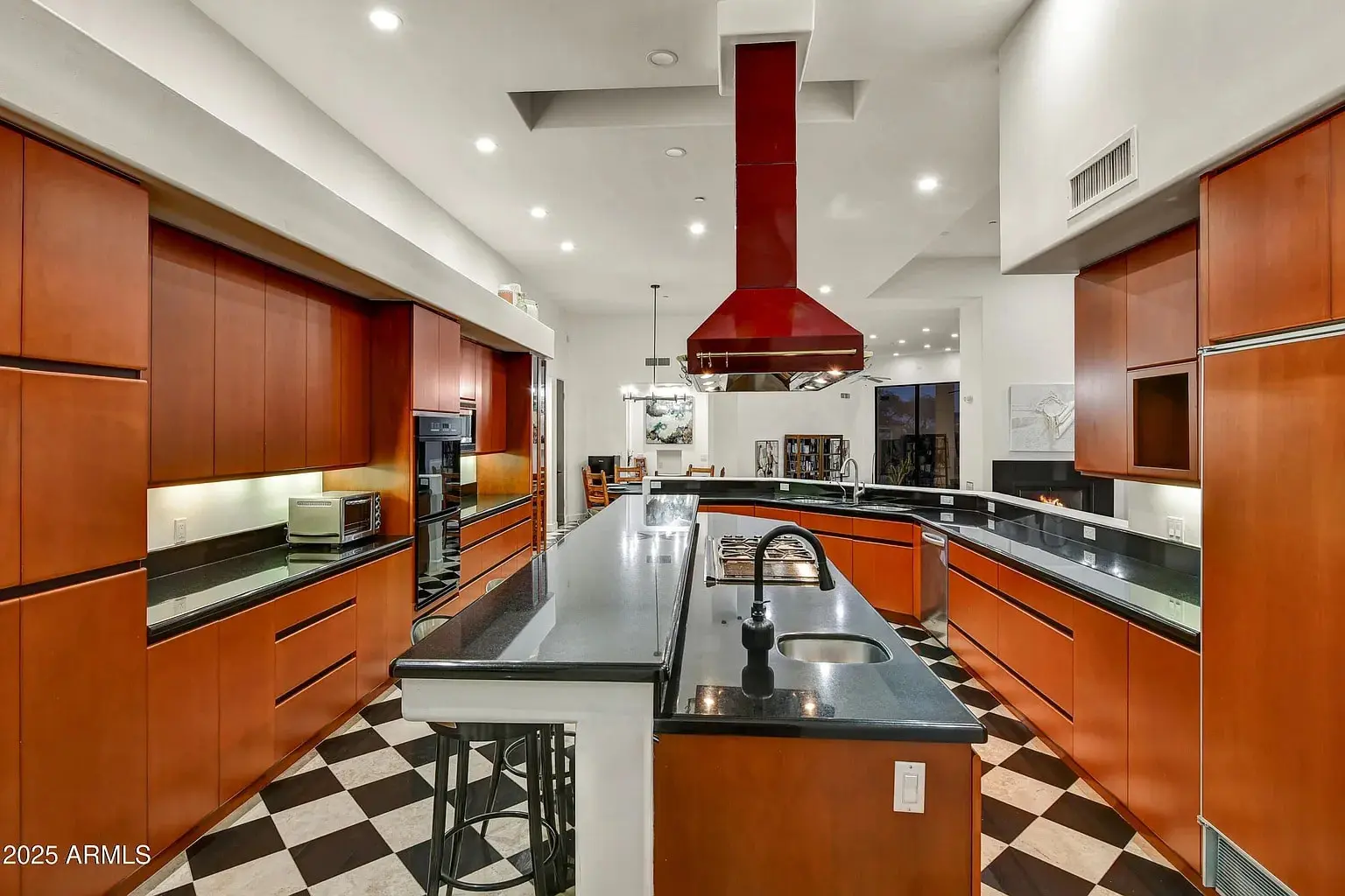 Modern kitchen with wooden cabinets, black countertops, red range hood, and checkered floor tiles.