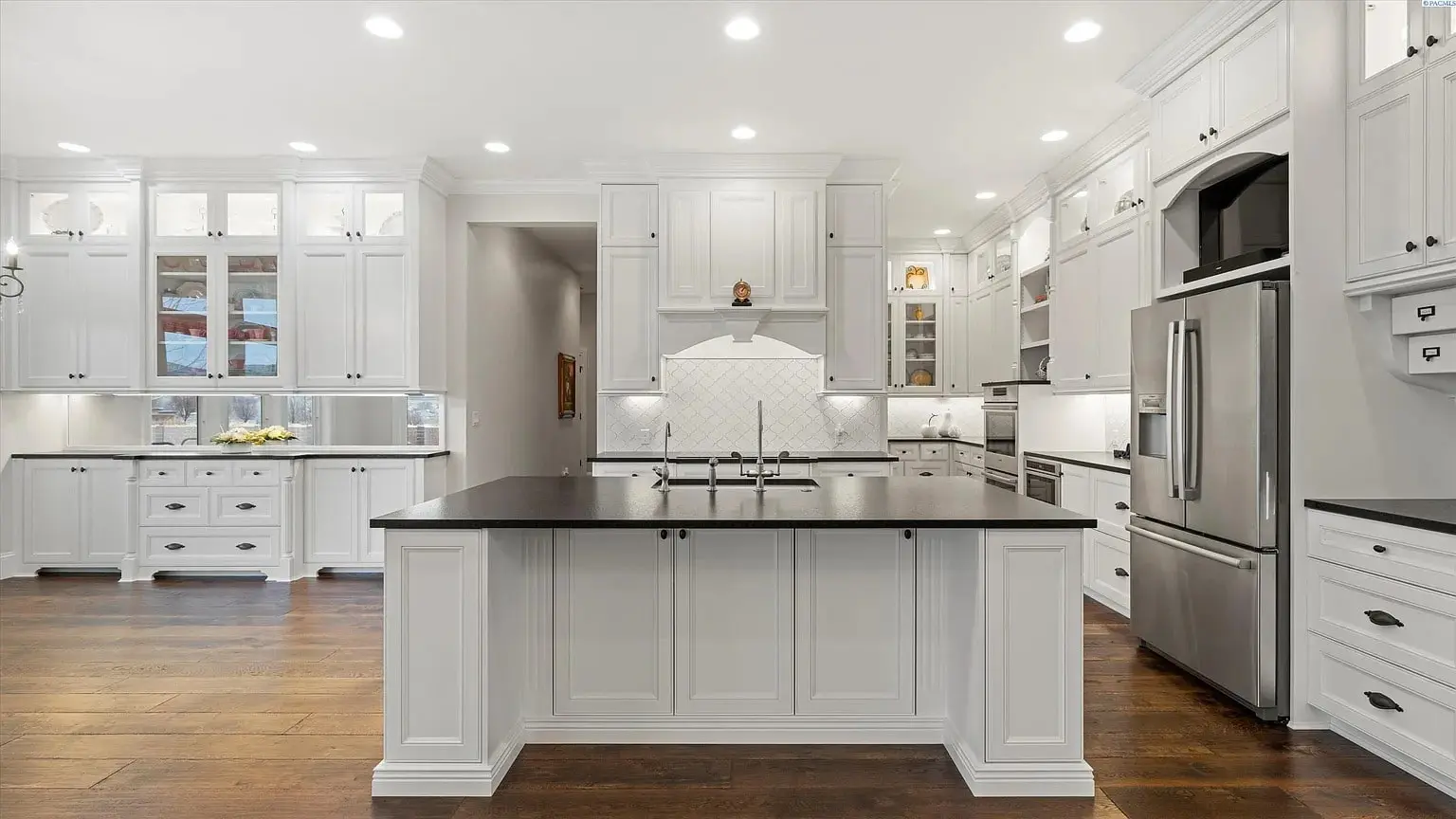 Modern kitchen with white cabinets, dark countertops, stainless steel appliances, and a central island.