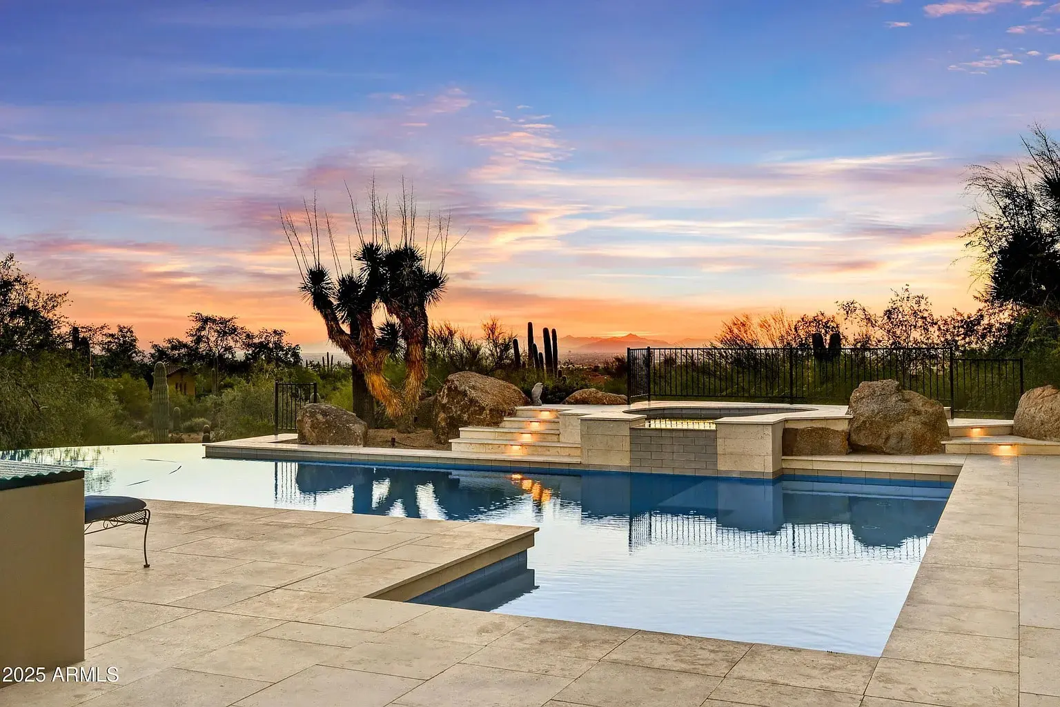 Luxurious pool and patio area with desert landscape at sunset, featuring cacti and rocks.